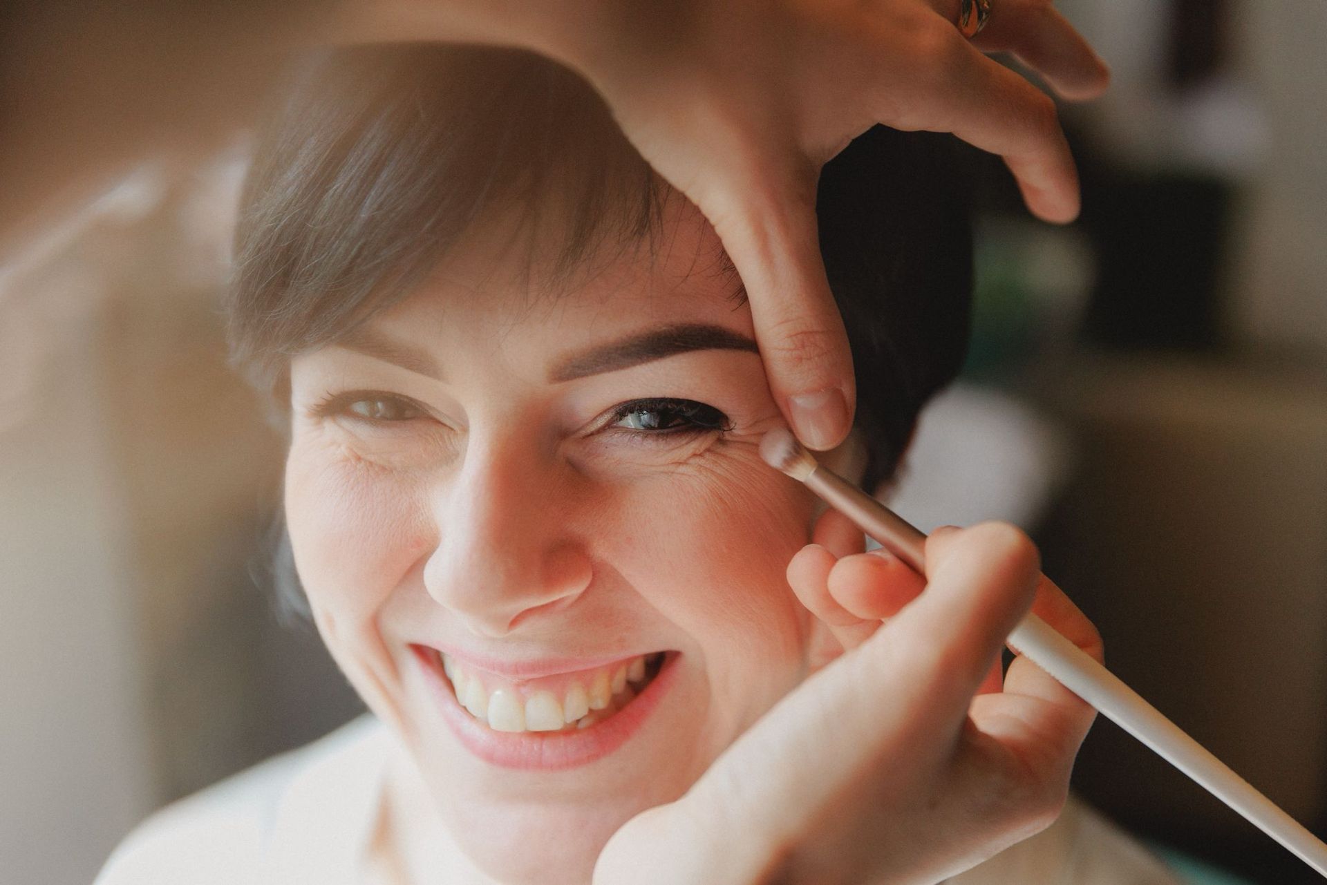 Un truccatore utilizza un pennellino per applicare il trucco sugli occhi di una persona sorridente.