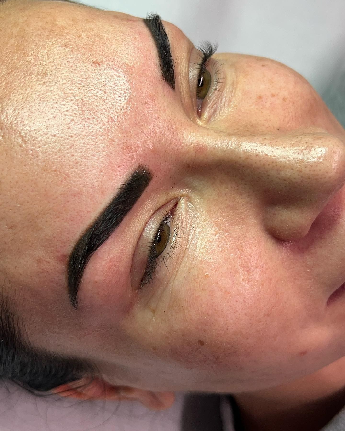 Primo piano di sopracciglia appena tatuate, scure e ben definite, sul viso di una persona.