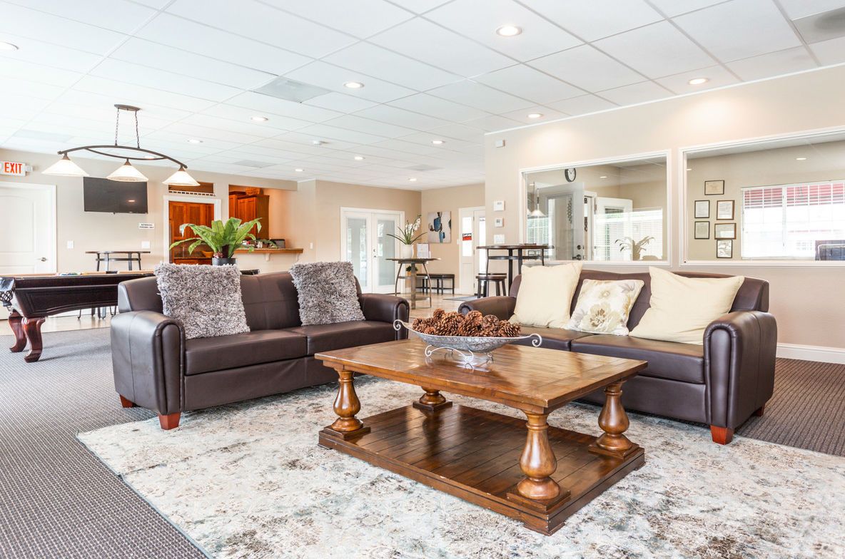 A lounge area with brown leather couches, coffee table, and a pool table in the background.