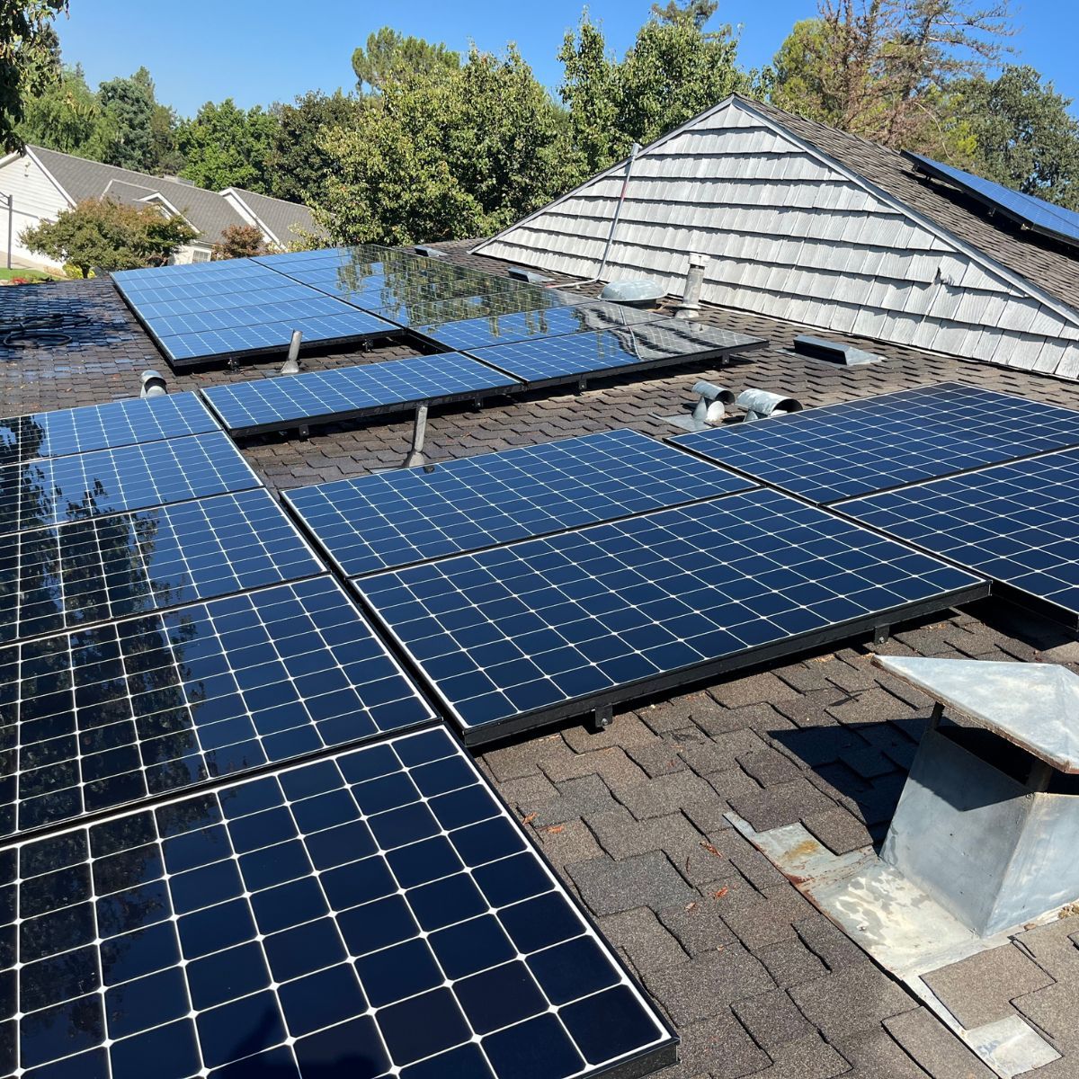Rooftop solar panels installed on a shingled roof under a clear blue sky.