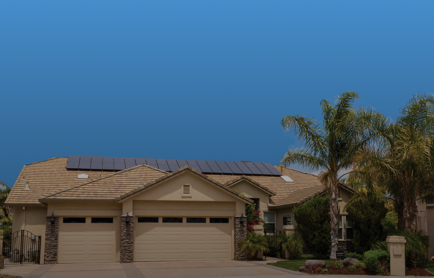 House with solar panels on roof, palm tree, blue sky.