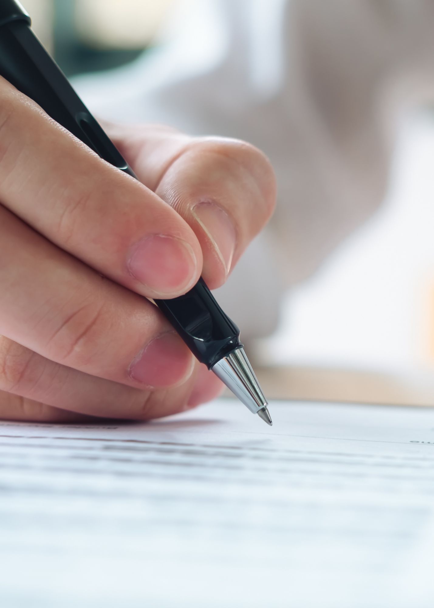 Hand holding a black pen, writing on lined paper.