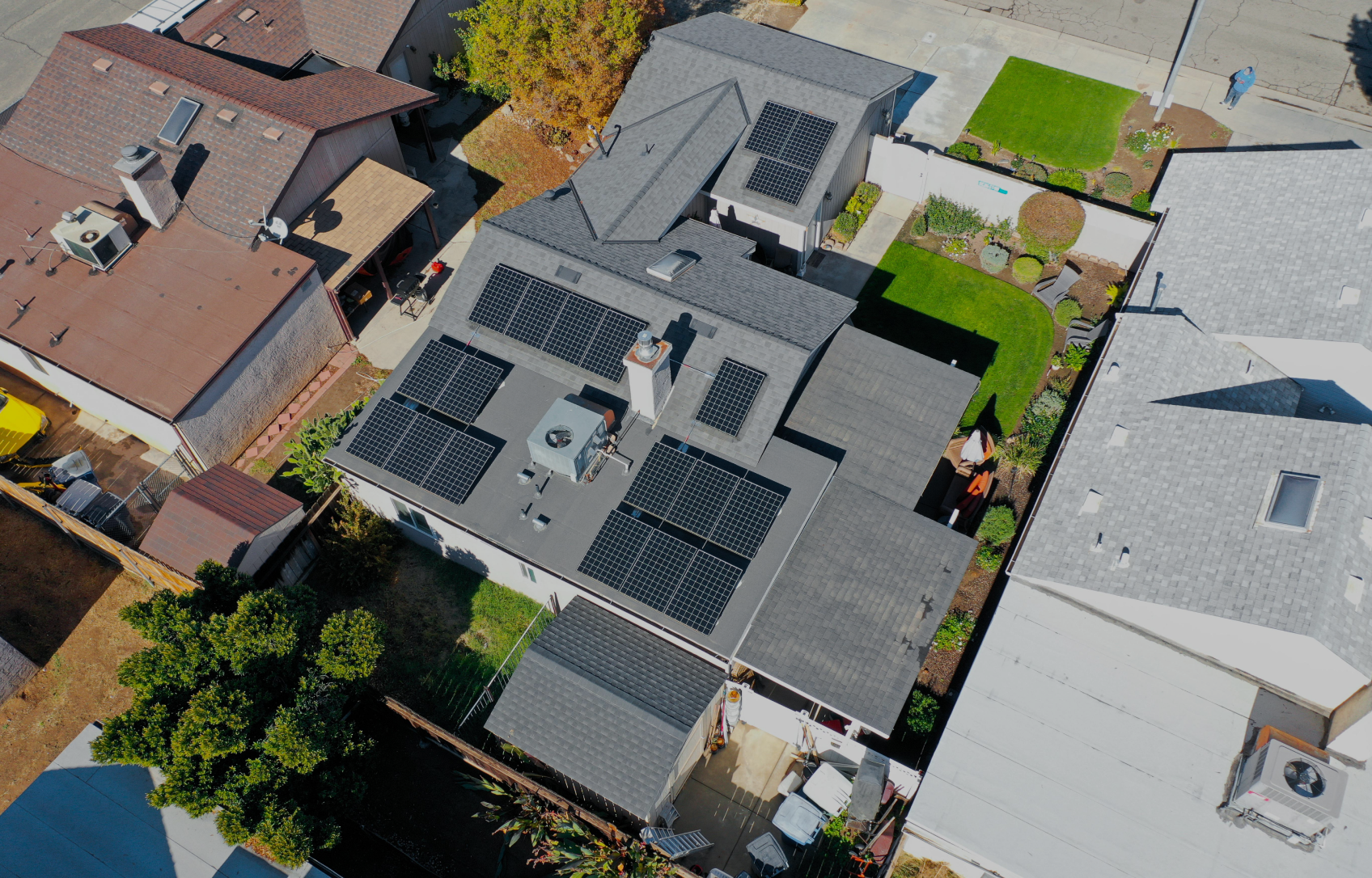 Aerial view of a house with solar panels on the roof surrounded by other houses and green lawns.