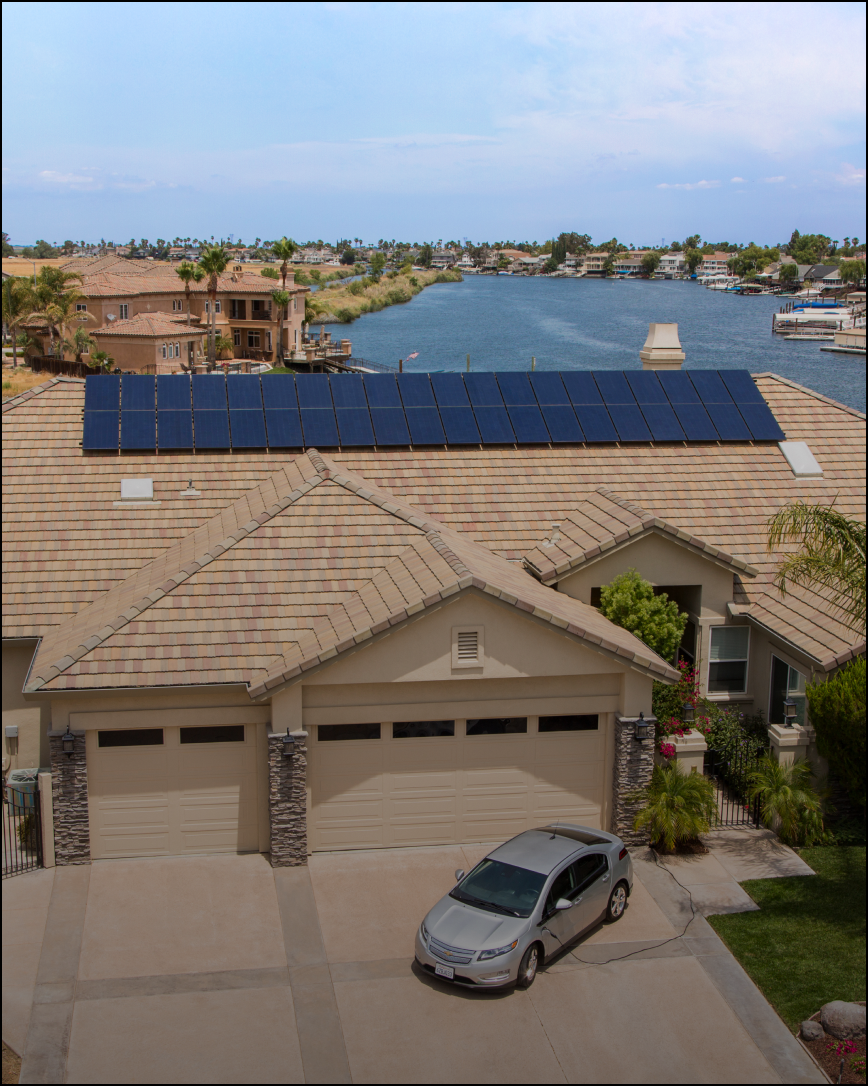 Residential house with solar panels on the roof, electric vehicle parked in the driveway, canal view.