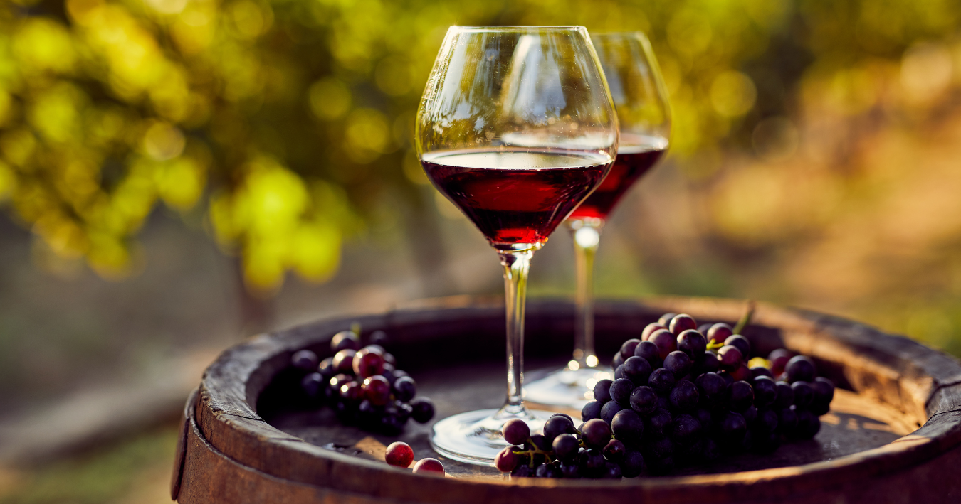 Wine glass on a rustic barrel with grapes, set outdoors in warm sunlight.