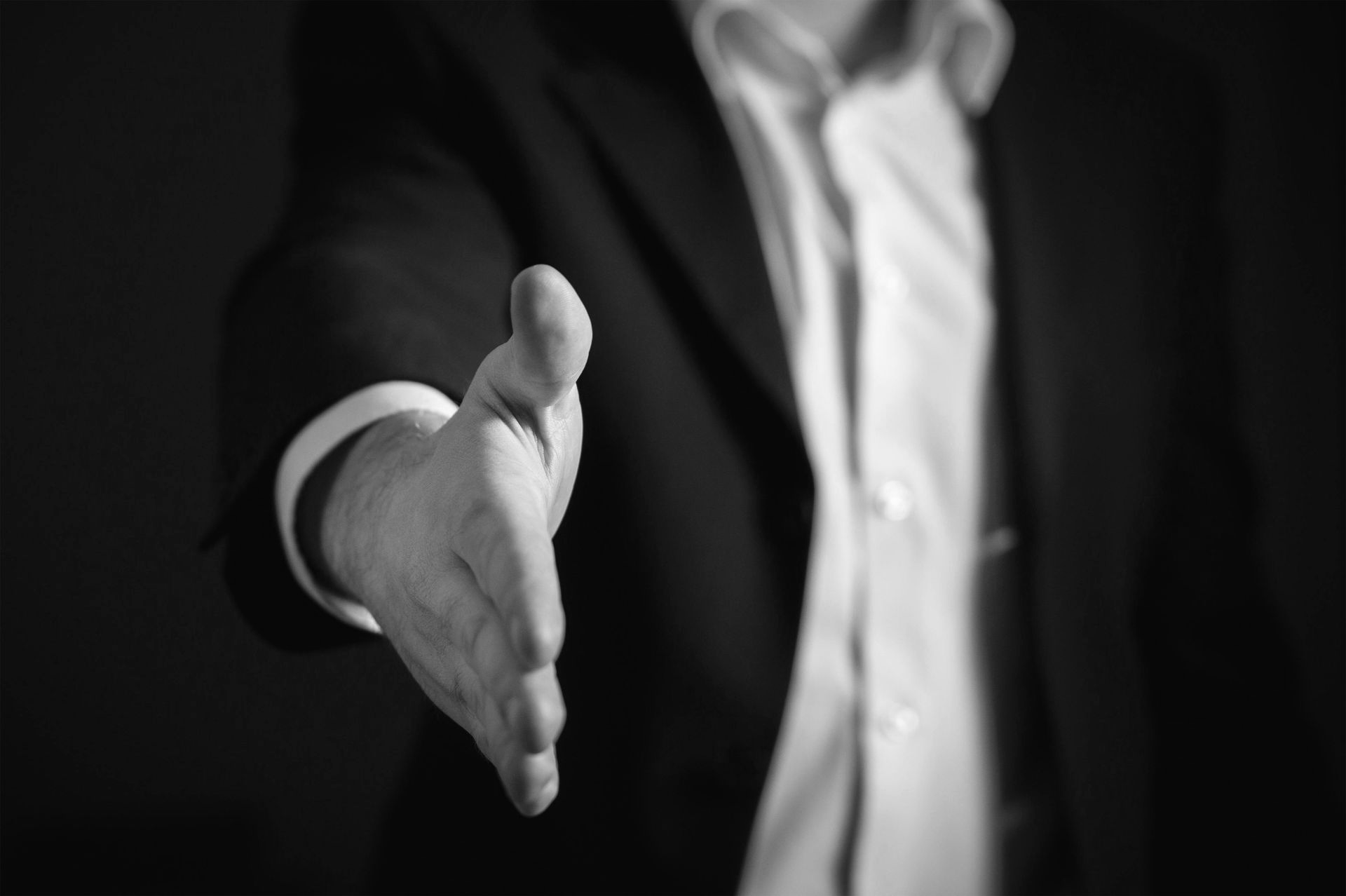Person in suit extends hand for a handshake. Black and white.