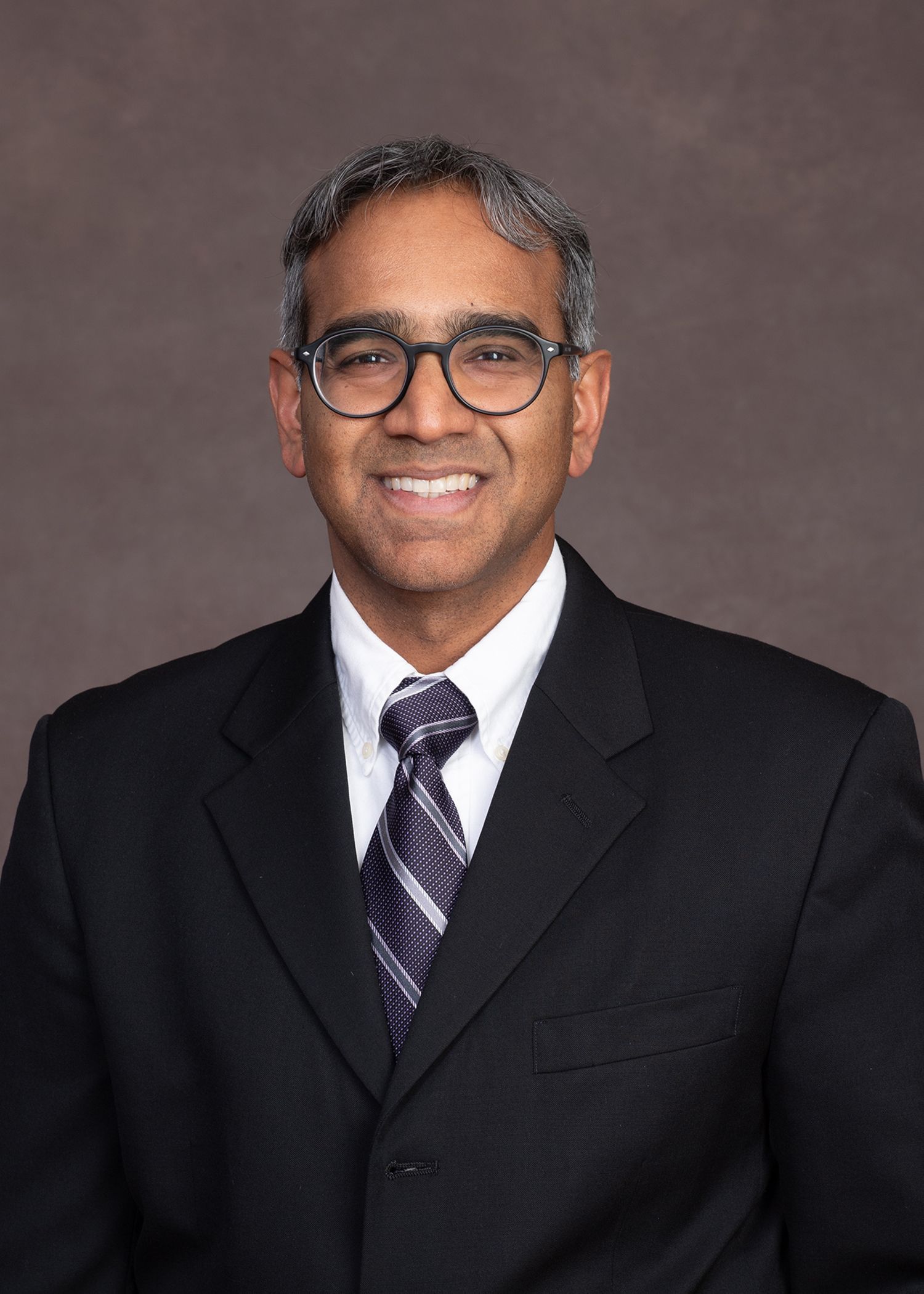 A smiling doctor in a lab coat with a stethoscope around his neck.