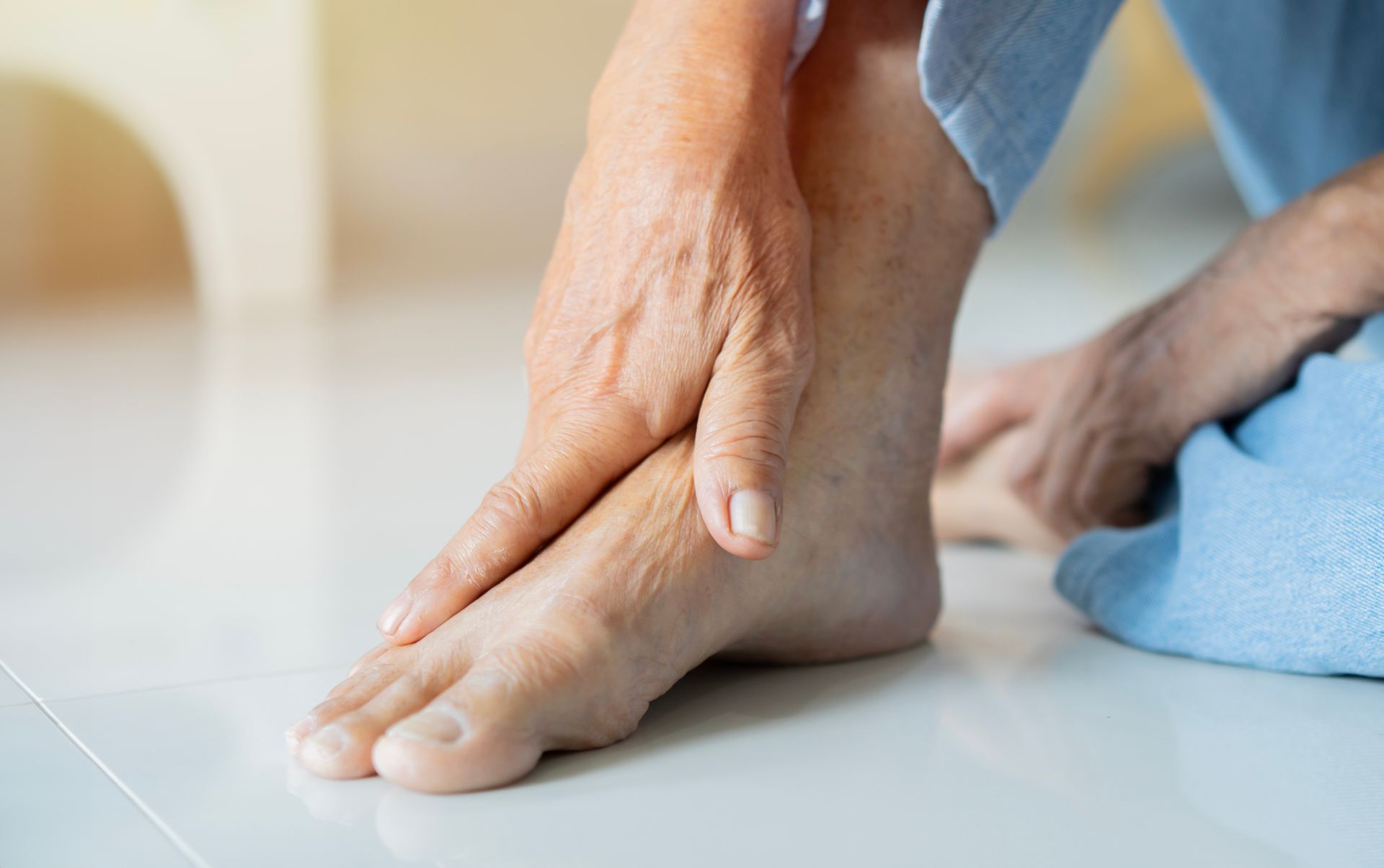 Person holding their hand on their foot, possibly due to pain or discomfort. Indoor setting, light skin tone.