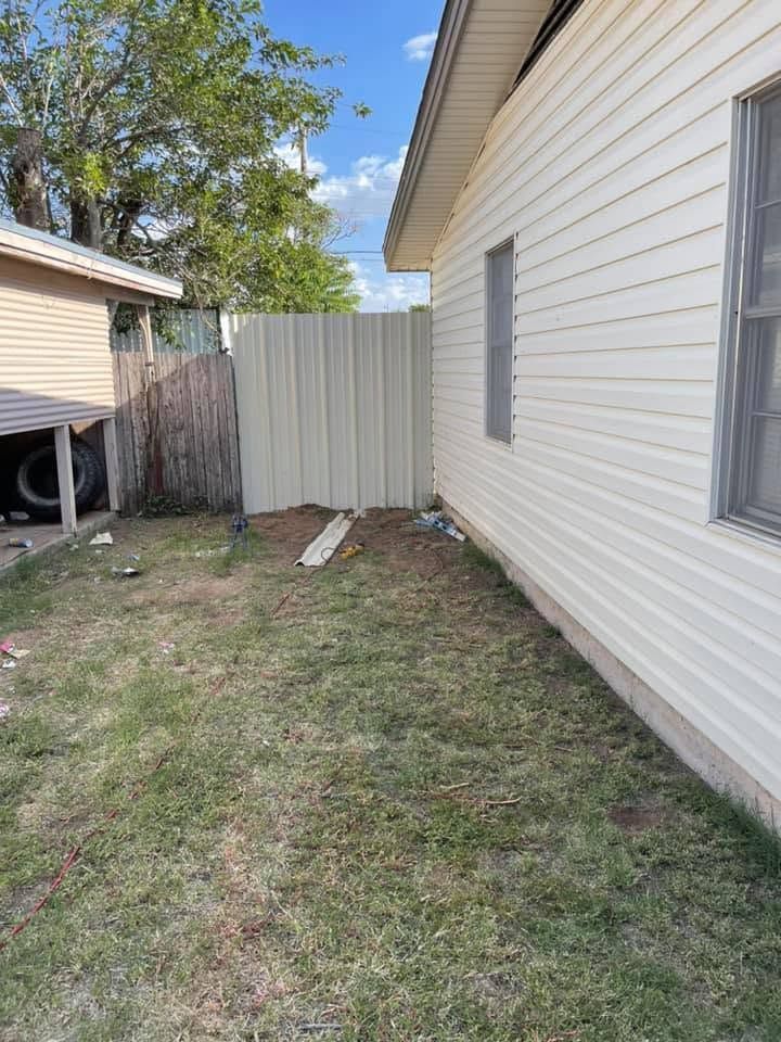 Narrow side yard beside a white house, with a fence, grass, and a small shed in the background