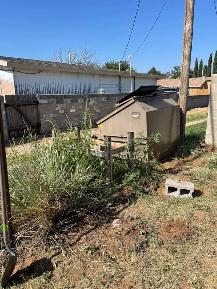 Backyard with a tan shed, tall grass, a utility pole, and a cinder block in the foreground