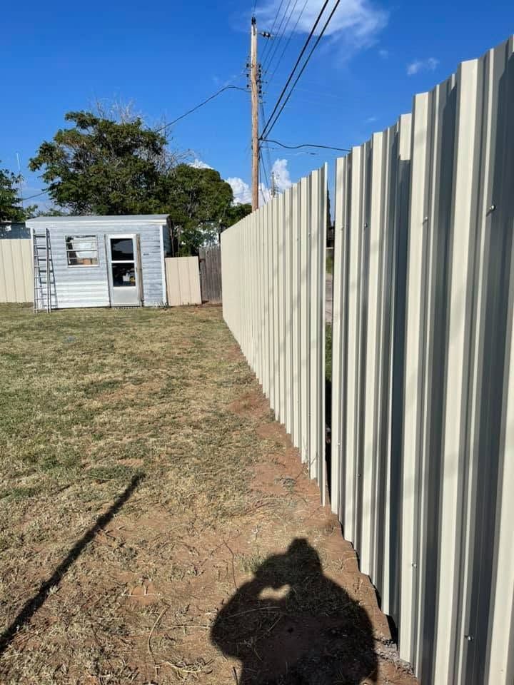 Backyard with a white shed, tall corrugated fence, and utility pole under a clear blue sky.