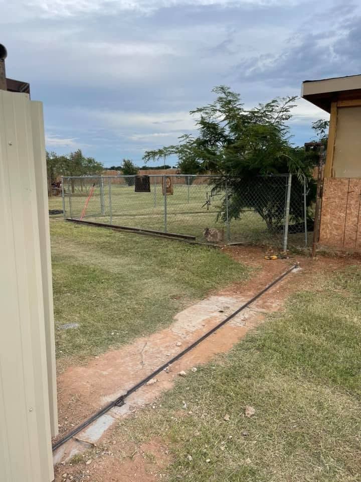 Backyard with a chain-link fence, grassy yard, and a concrete path beside a building.