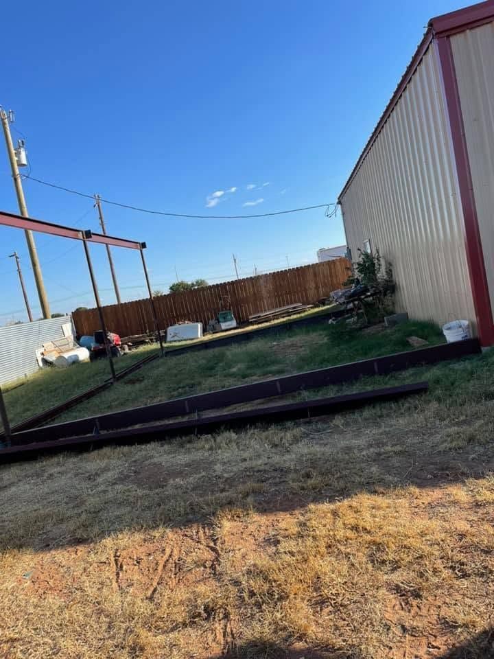 Backyard with dry grass, a shed, fence, and clear blue sky under construction poles