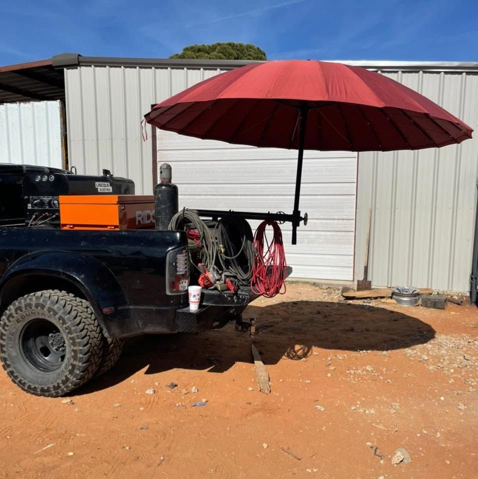 Black truck with red umbrella and gear parked beside a metal shed in a dusty yard