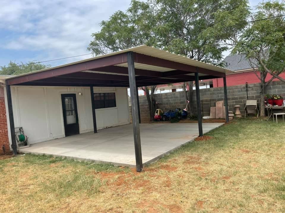 Small covered patio with metal roof beside a white house and grassy yard.