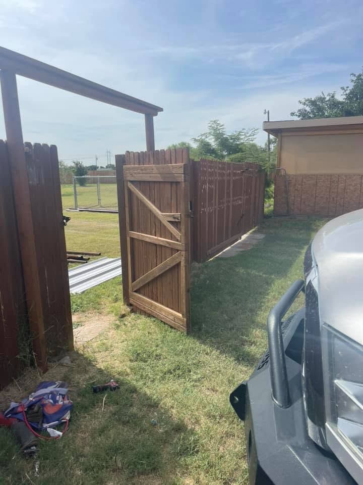 Open wooden gate beside a parked car, with a grassy yard and backyard fence in sunlight.