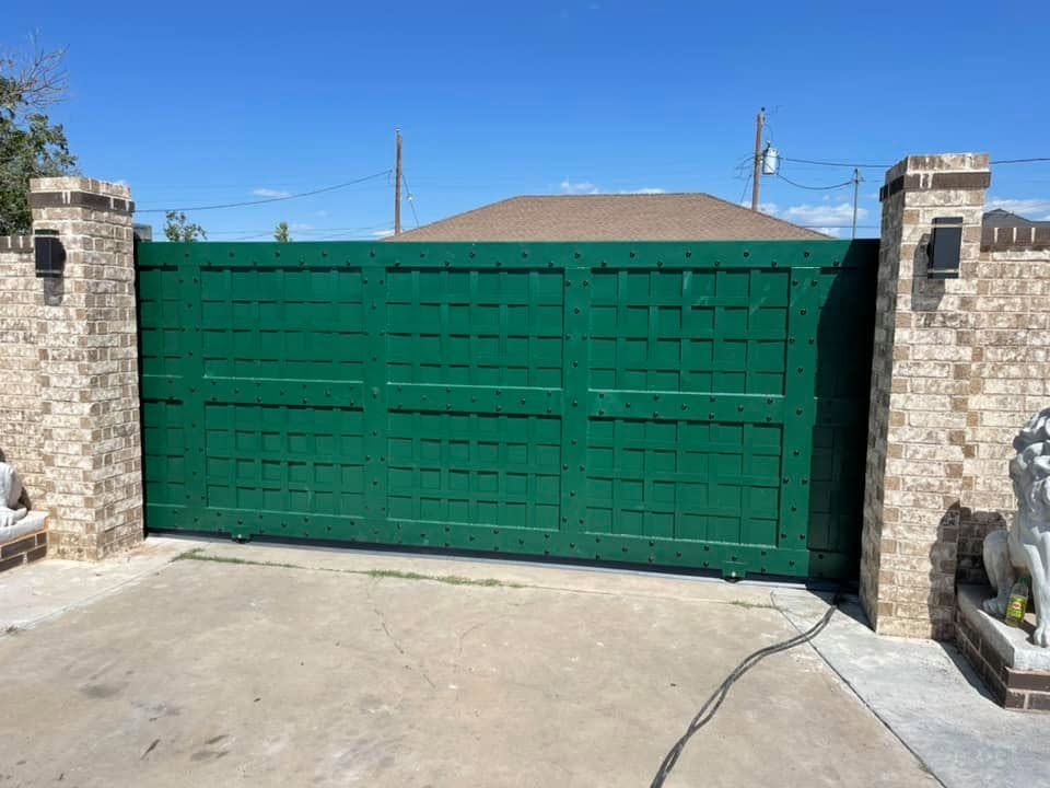 Green driveway gate between stone pillars under a clear blue sky.