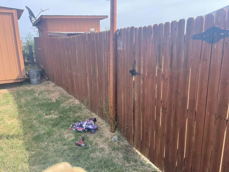 Wooden backyard fence beside a grassy yard and shed, with a small pile of clothes on the ground