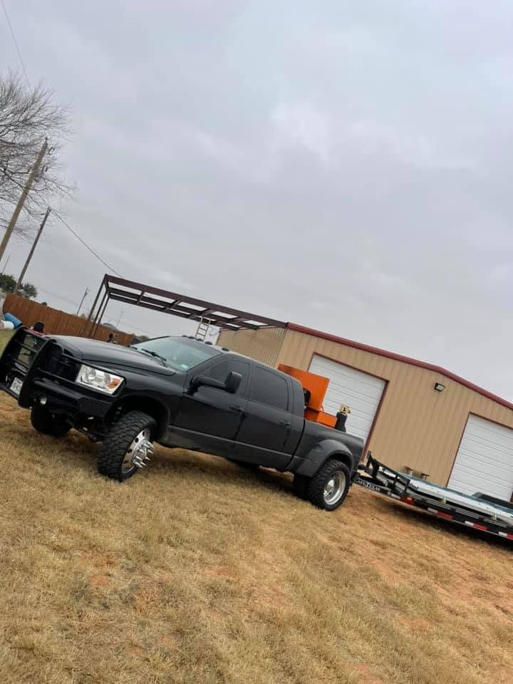 Black lifted pickup truck parked on a grassy lot beside a beige warehouse under an overcast sky.