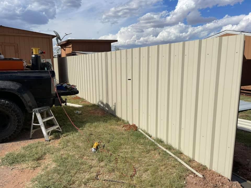 Tan metal fence panels installed along a grassy yard beside a house and vehicle