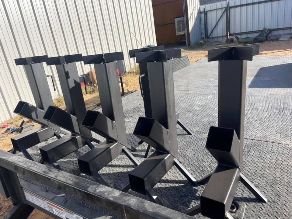 Row of black metal outdoor stove stands on a gravel lot beside a fence and building.