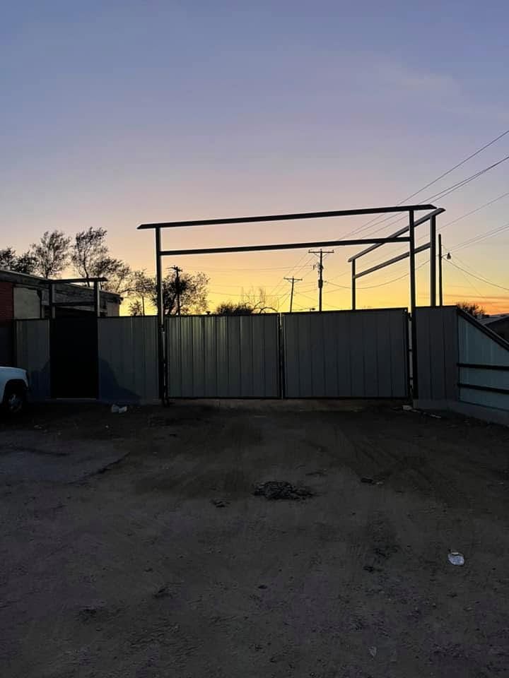 Empty lot with a large metal gate at sunset, silhouetted against a fading purple-orange sky.