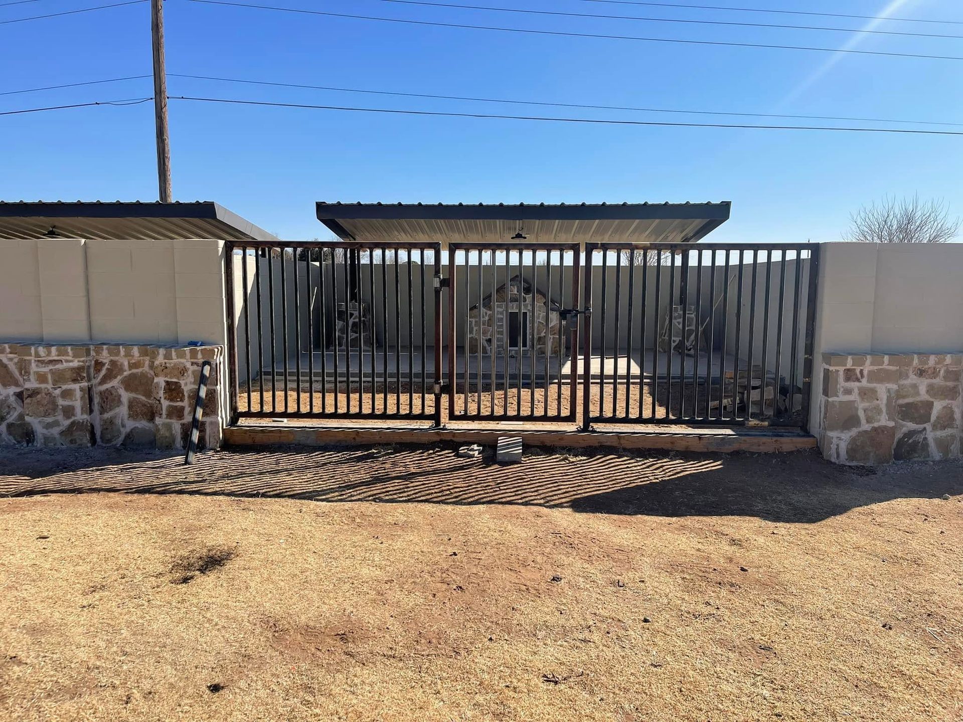 Front gate of a stone wall and metal fence surrounding a property under a clear blue sky
