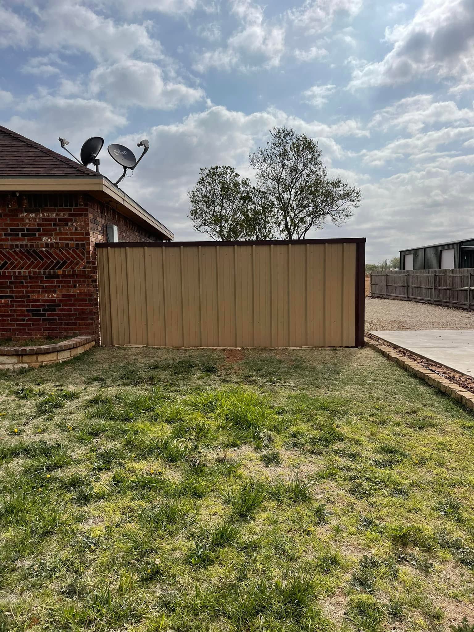Backyard with a tan fence, brick house corner, tree, and cloudy sky