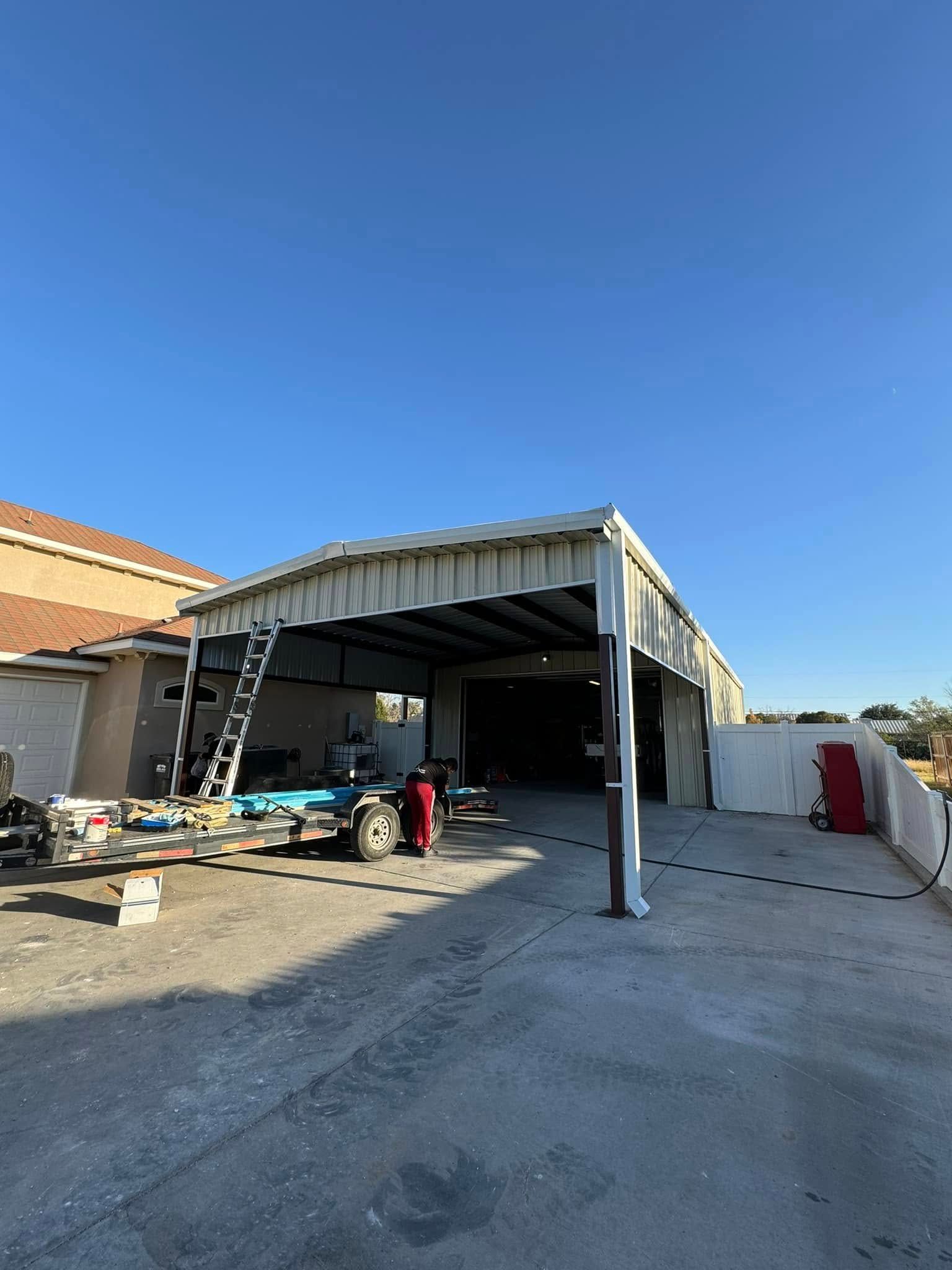Partially collapsed carport with a damaged awning, tools and debris in a driveway under a clear blue sky