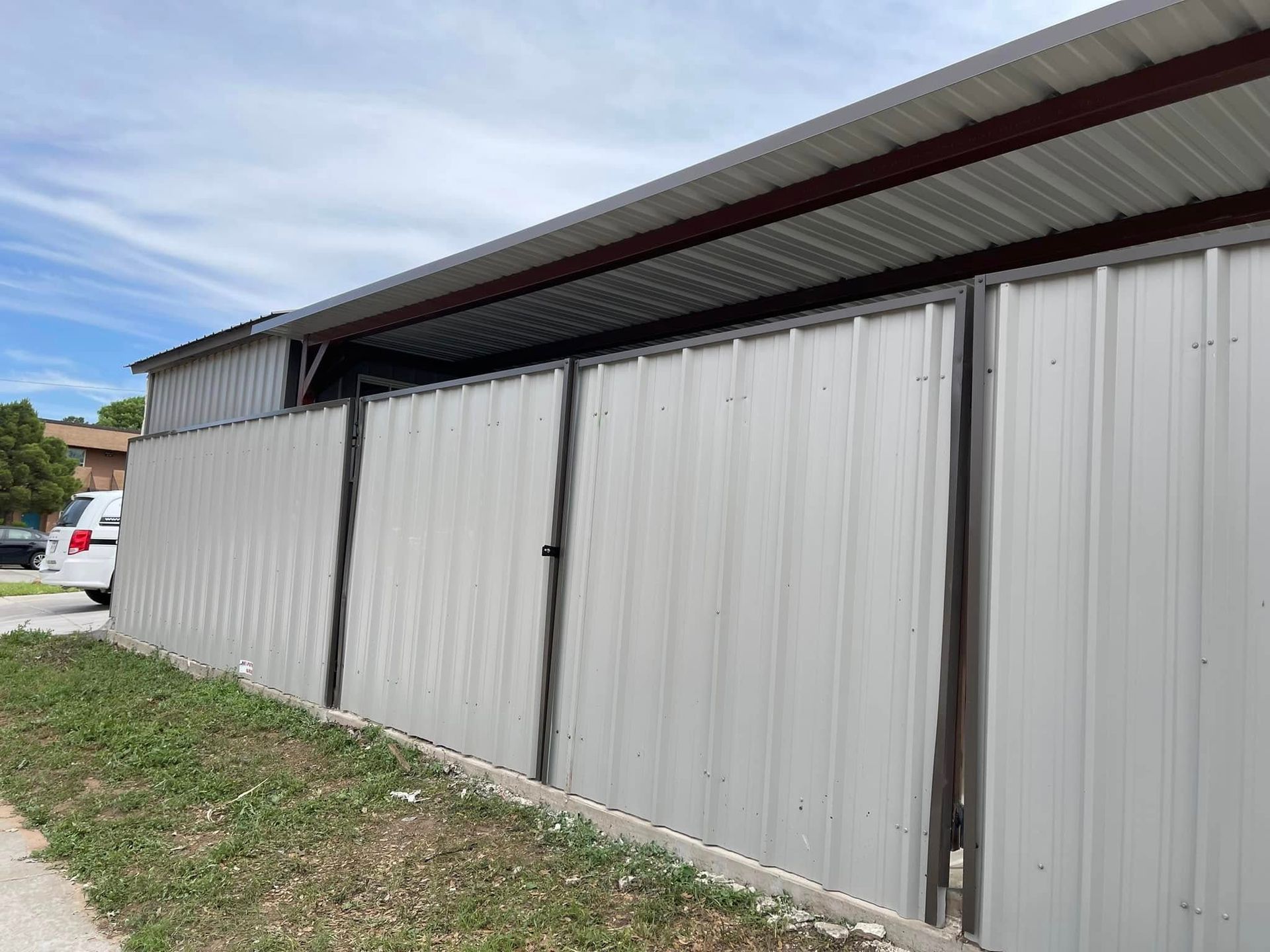 Long gray corrugated metal shed or garage with a slanted roof beside a grassy roadside.