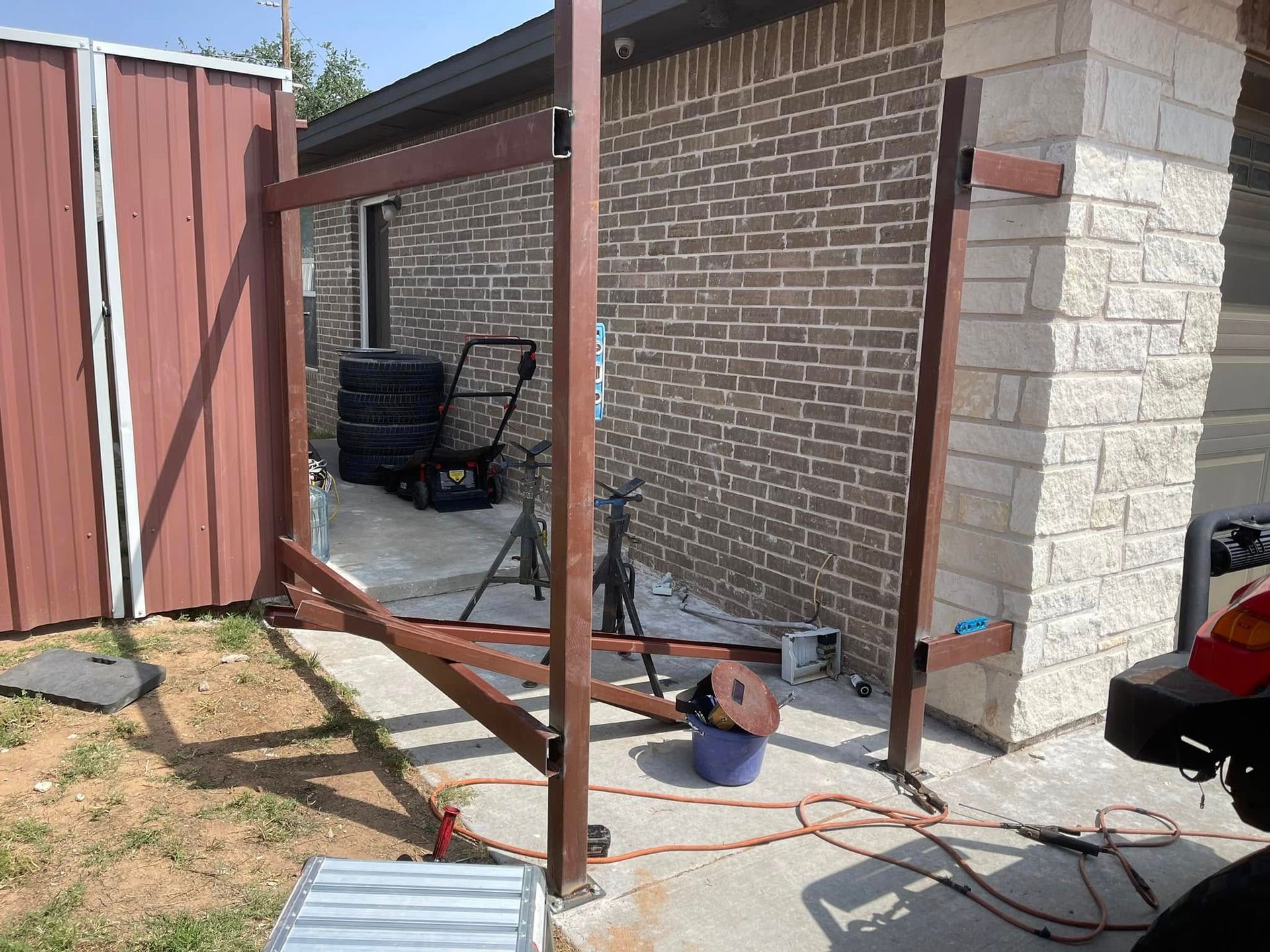 Partially built patio frame beside a brick house with tools and cords on the ground