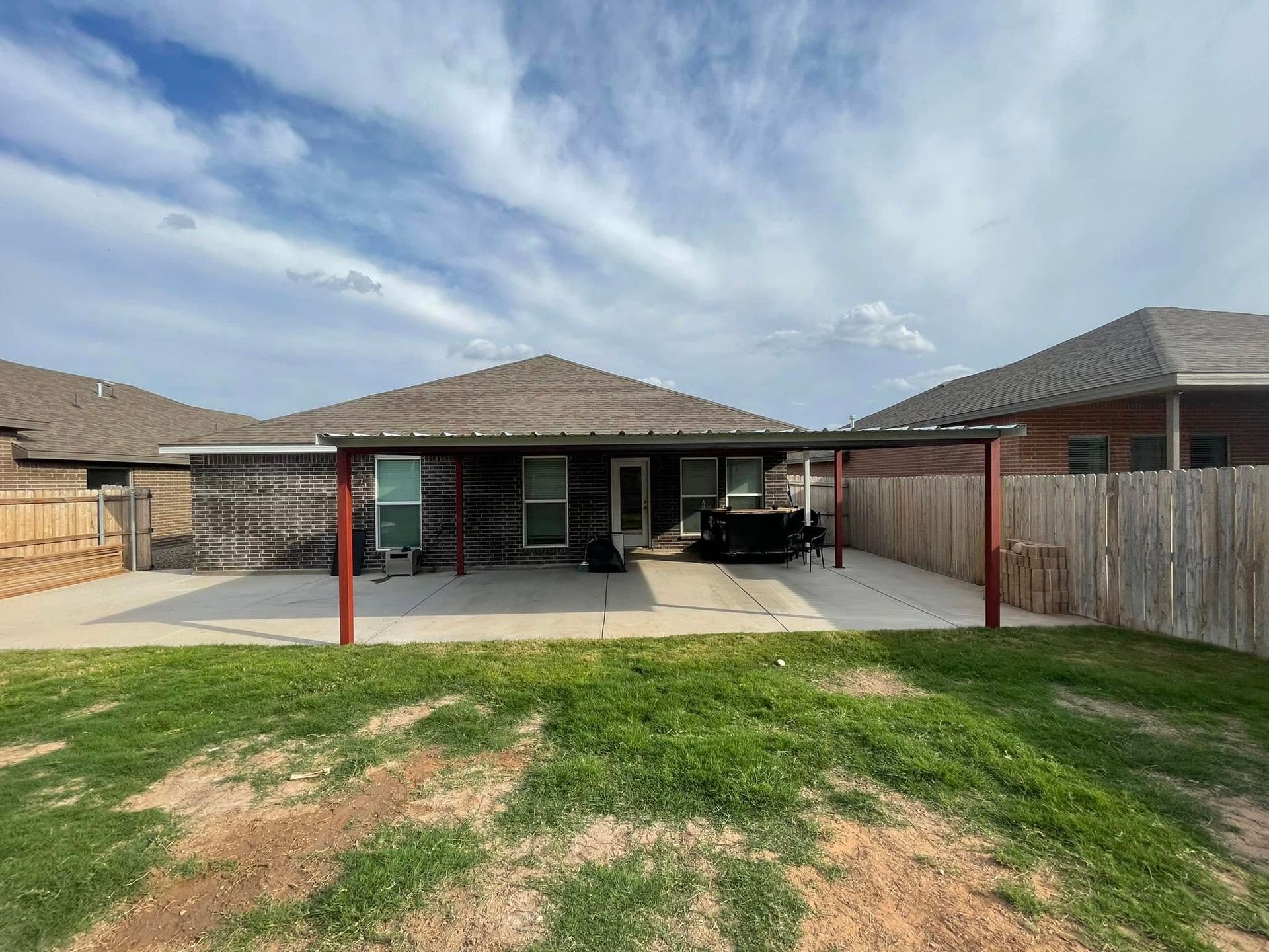 Backyard patio with covered seating, concrete slab, grass lawn, and a fenced suburban home.