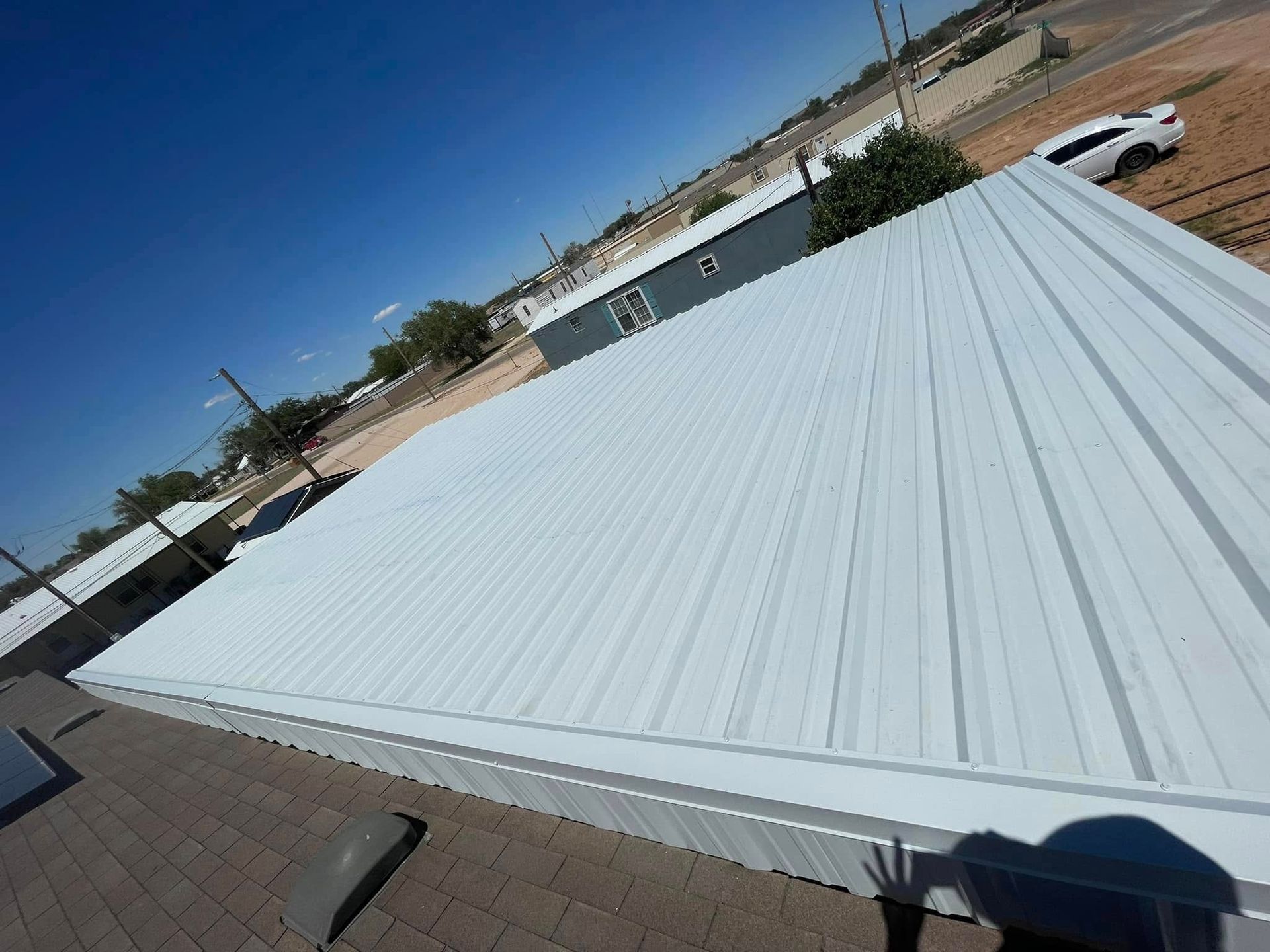 White metal roof on a building under a clear blue sky, with desert surroundings and parked vehicles nearby