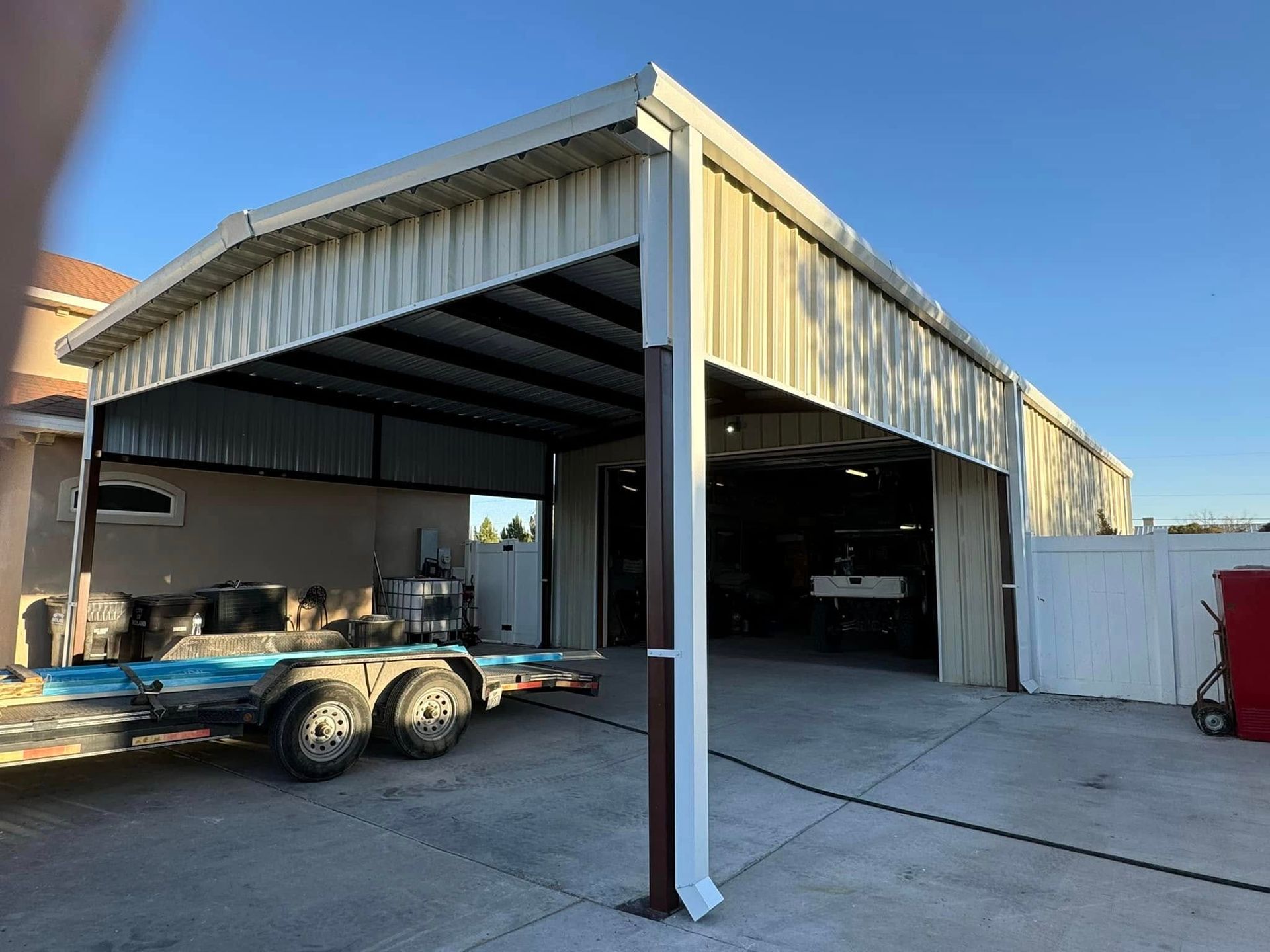 Open metal-sided workshop with a truck trailer parked at the entrance under a blue sky