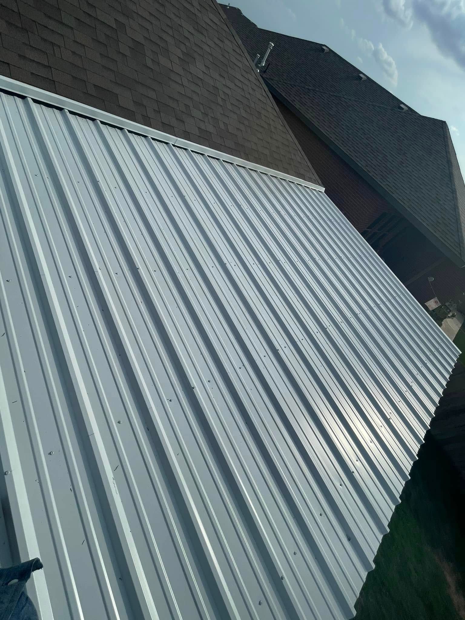Tilted view of a corrugated metal roof against a brick building and cloudy sky
