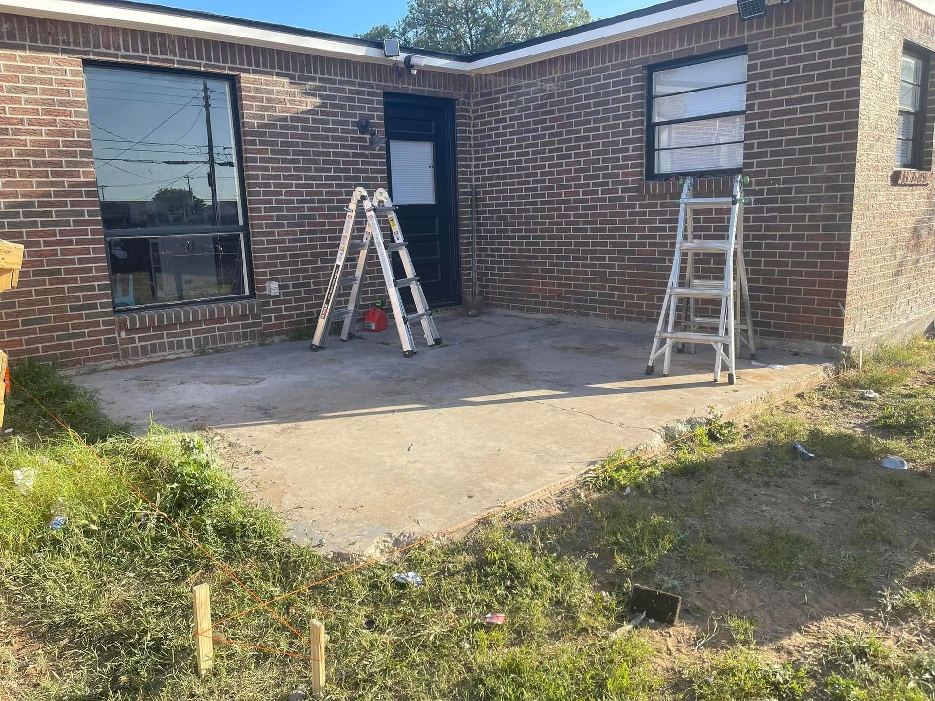 Brick house patio with two ladders near the front door and a concrete slab in the yard