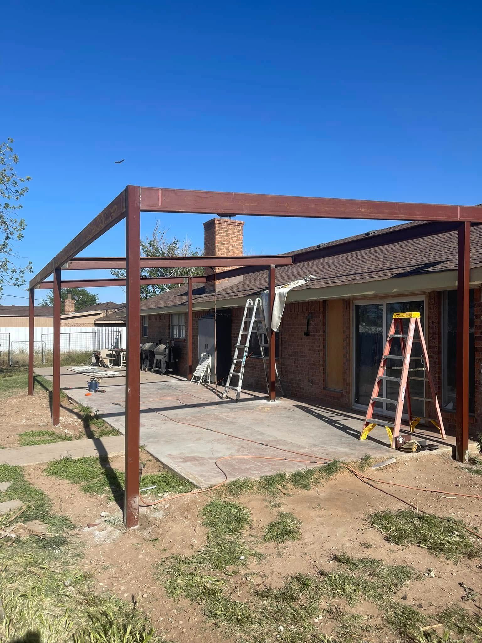 Backyard patio under construction with a rust-colored steel frame, brick house, and ladder under a clear blue sky