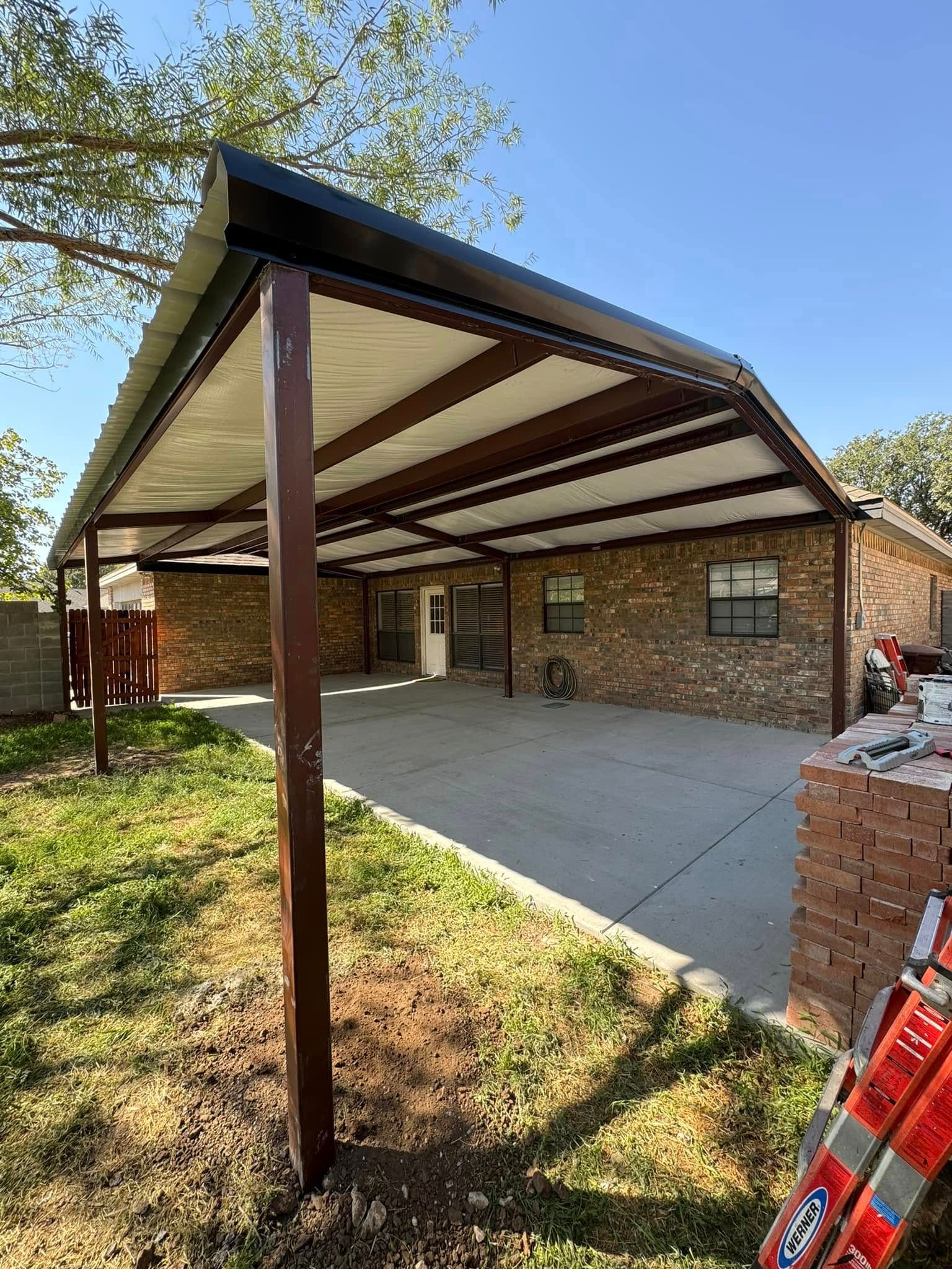 Covered carport with brick house, concrete driveway, and grassy front yard under a clear blue sky