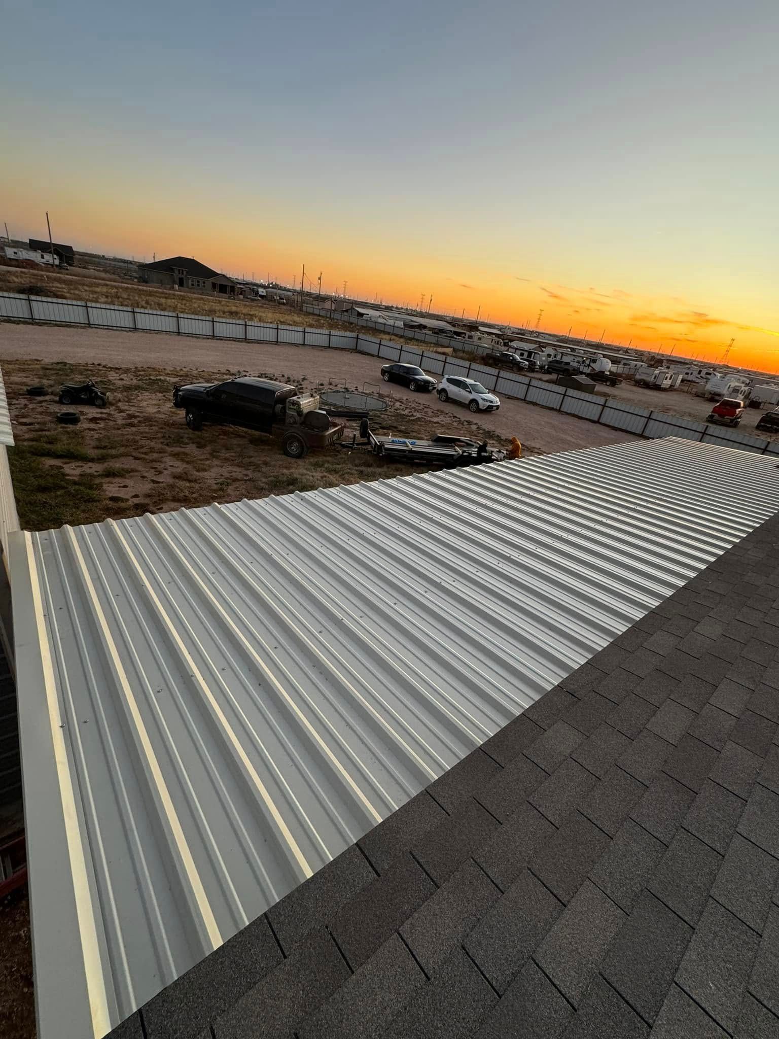 Sunset over a sloped rooftop with corrugated metal panels and distant houses on the horizon
