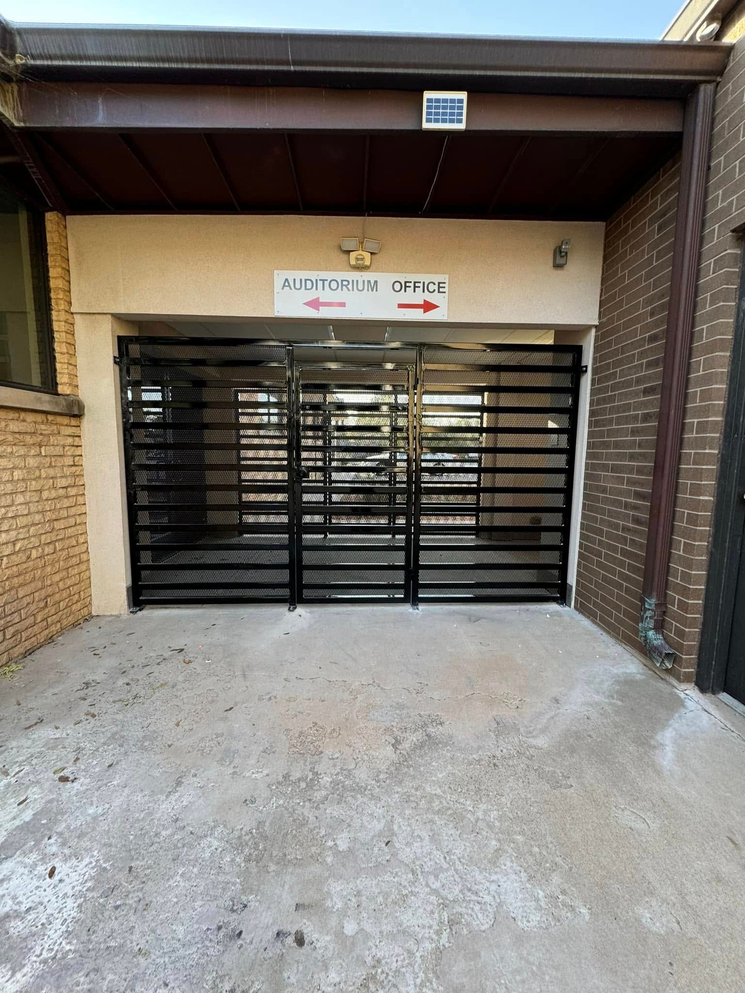 Black metal security gate at a building entrance with a sign above and gravel driveway in front