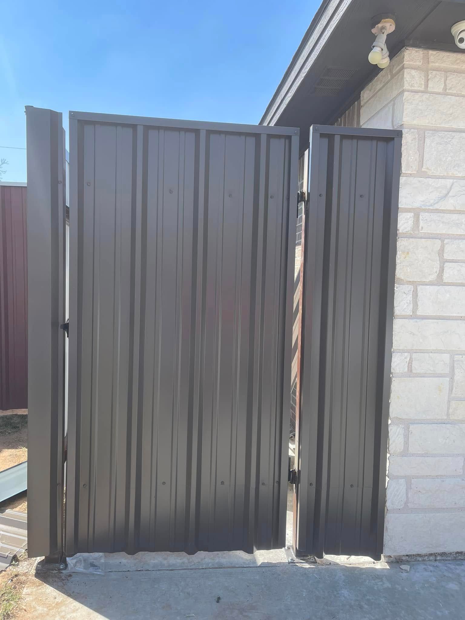 Tall dark metal gate beside a stone house wall under a blue sky