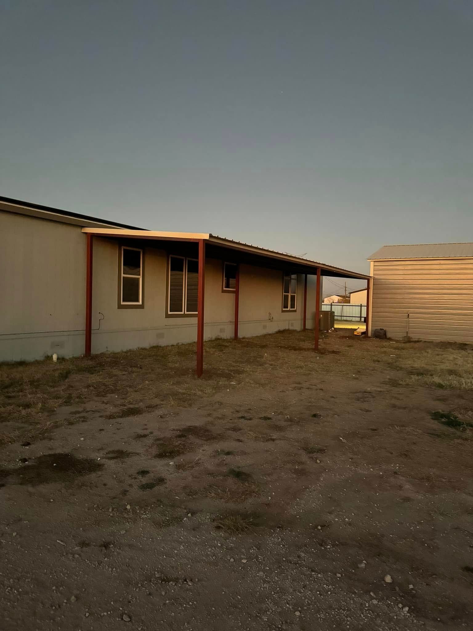 Single-story house and outbuilding in a gravel yard at dusk, with a dim sky overhead.