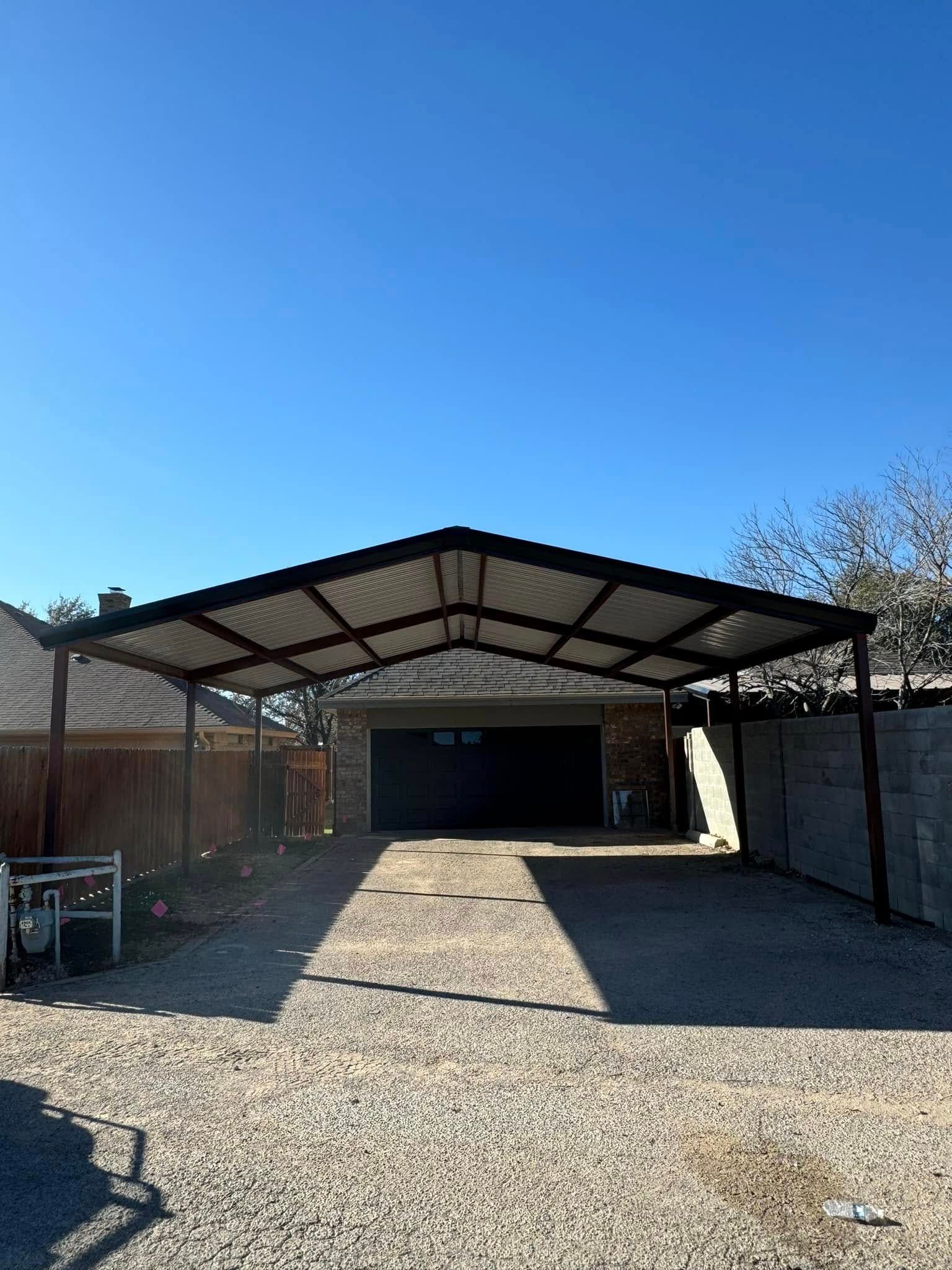 Gravel driveway leading to a metal carport and garage under a clear blue sky