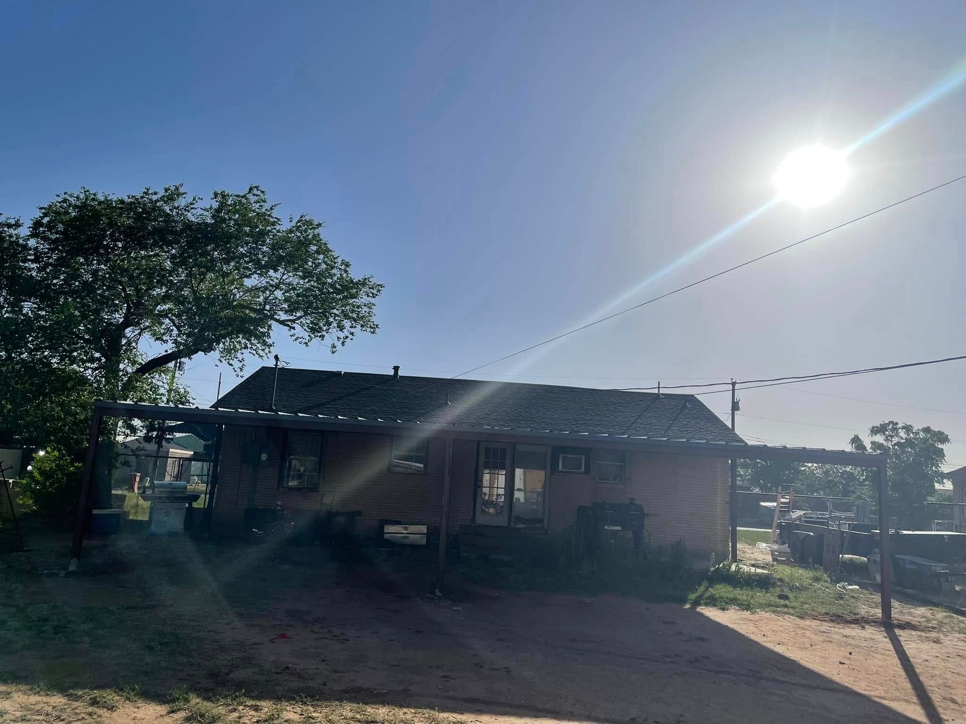 Small house in bright sunlight with trees and a dirt yard, viewed from the front.