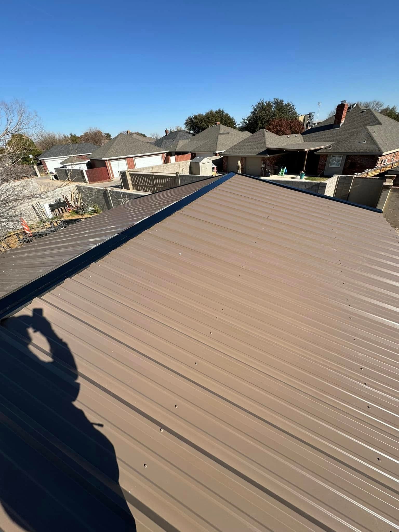 Ribbed metal roof with a shadow in the foreground, viewed over a suburban neighborhood on a clear day
