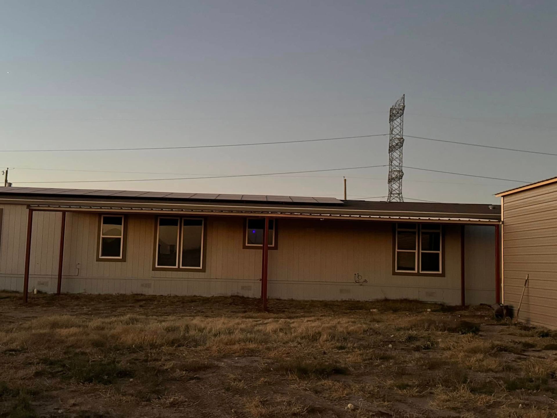 Single-story beige house with a flat roof and small windows in a dry yard at dusk