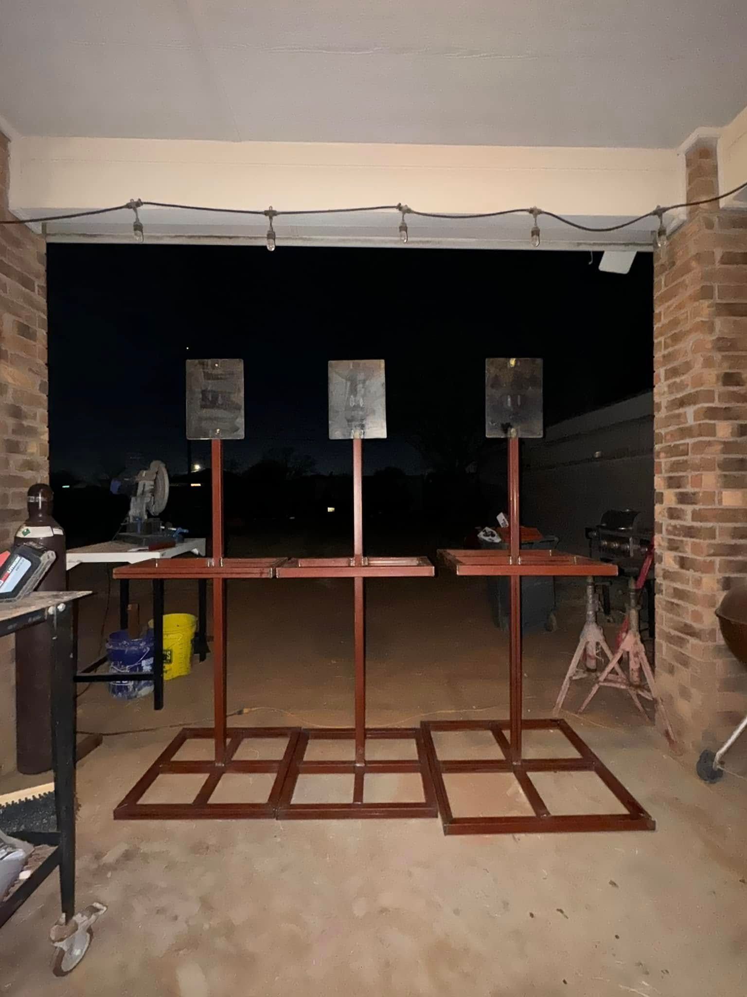 Indoor shooting range with three target stands and stools on a concrete floor.