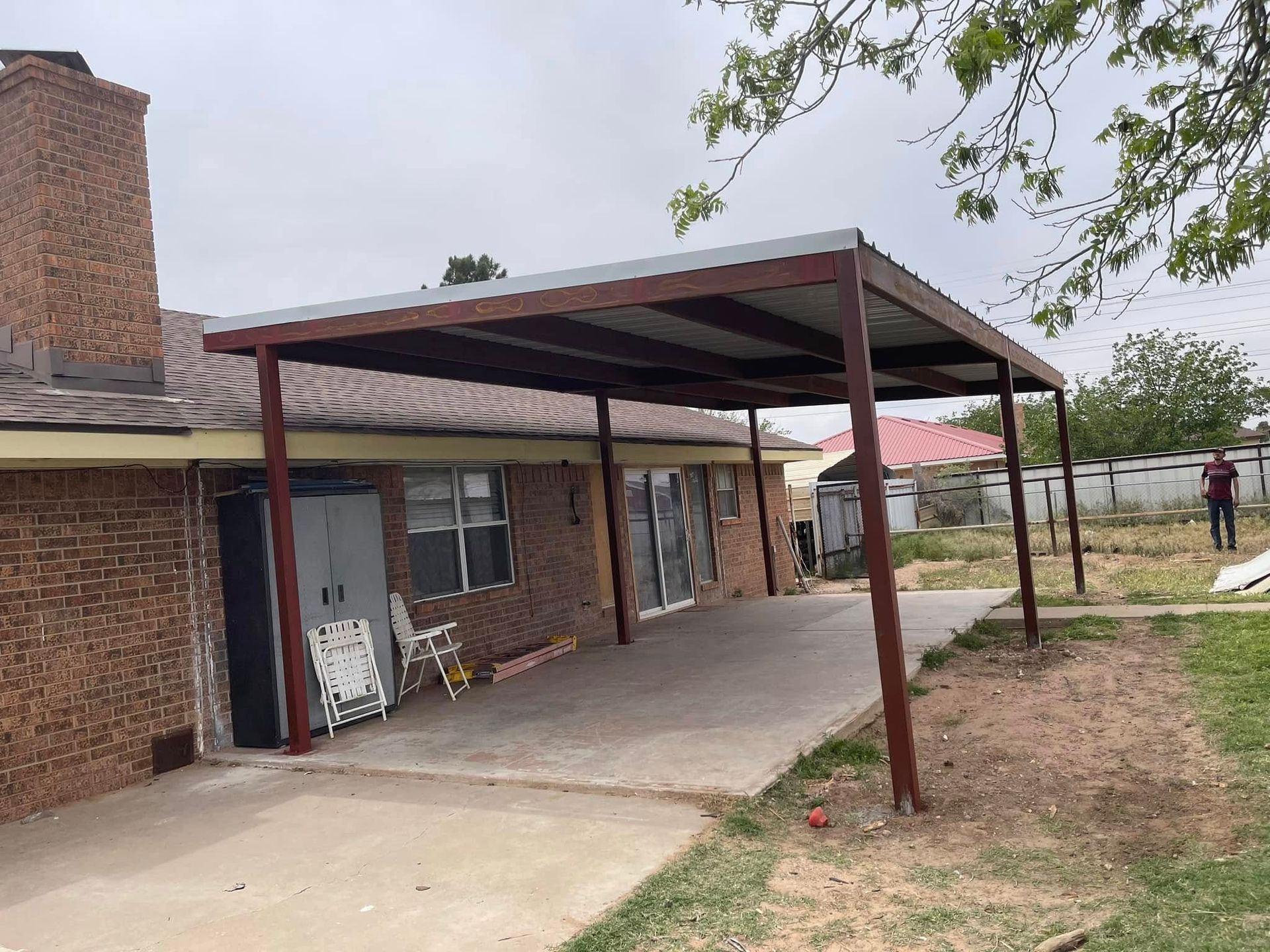 Brick house with a red metal carport and concrete driveway in a rural yard.