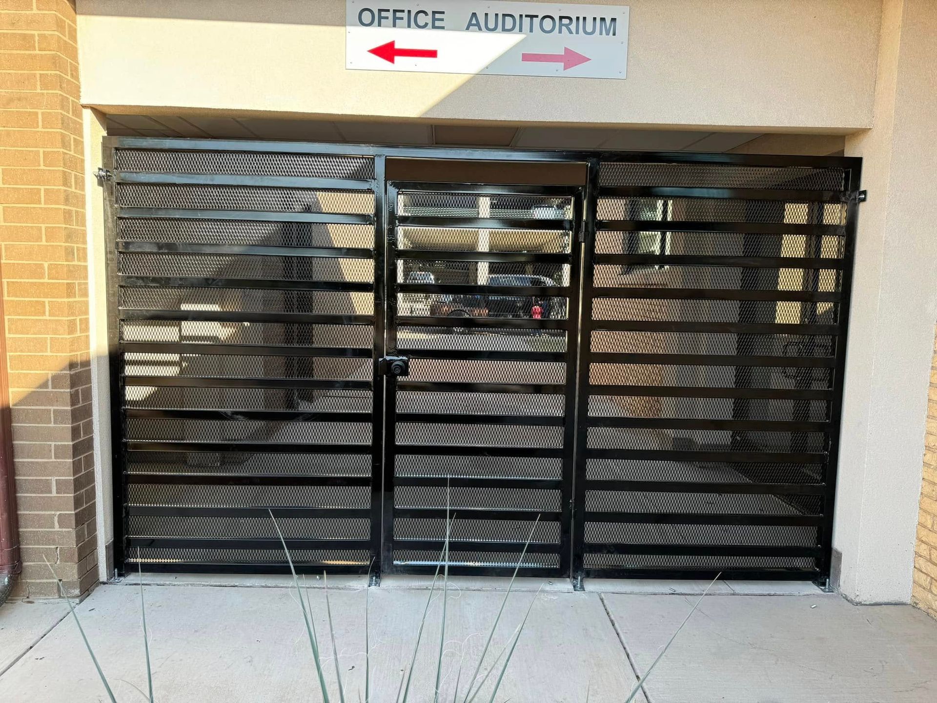 Black metal gate entrance beneath an “Office Auditorium” sign with arrows pointing left and right
