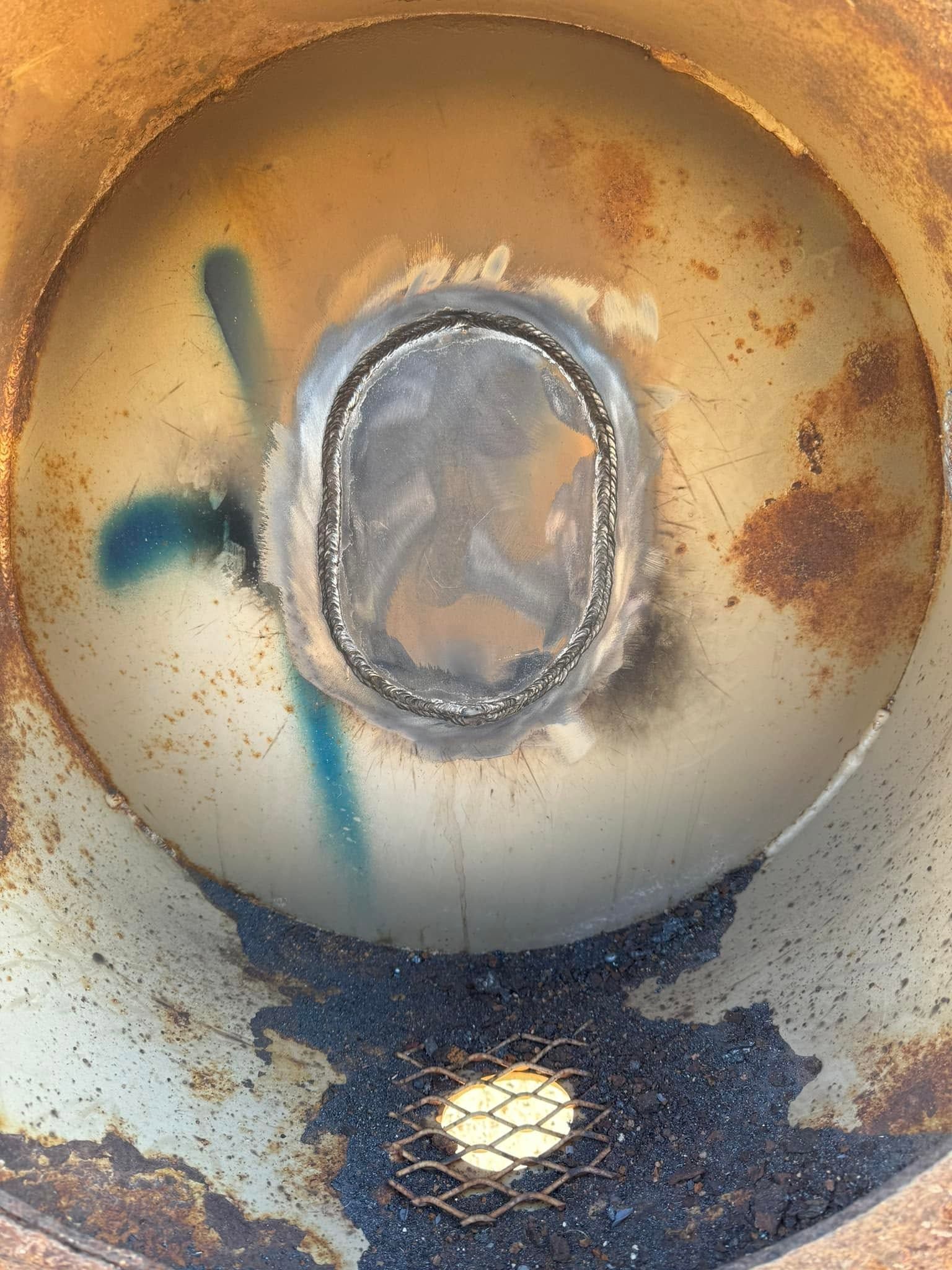 Rusty metal interior with a central oval opening and dark stains near the bottom